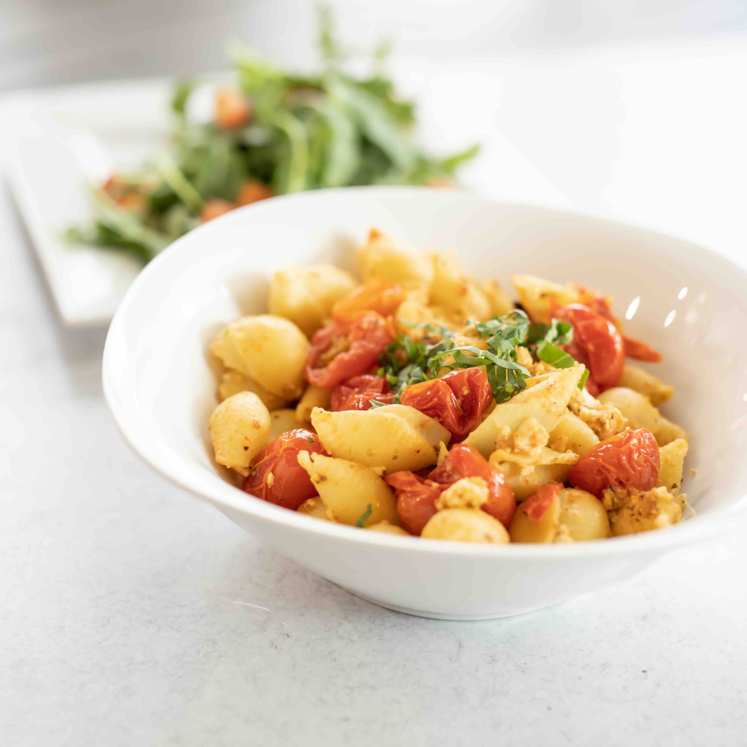 Pasta Dish with tomatoes and a salad in back 