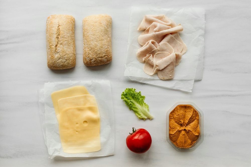 Briosche bun, turkey, cheesee, lettuce, tomato on a white table
