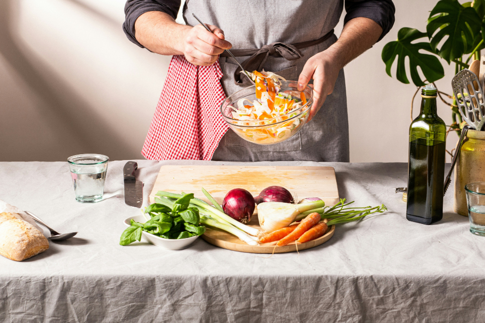 A mom stiringingredients in a bowl with celery, onions and carrots sitting on a counter.